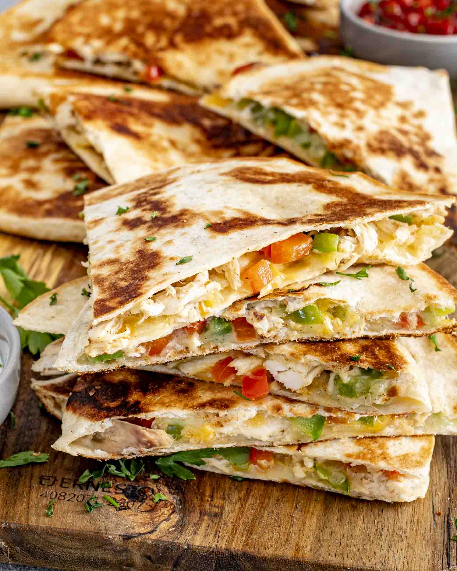 a stack of chicken quesadillas on a board with a bowl of salsa in the background.