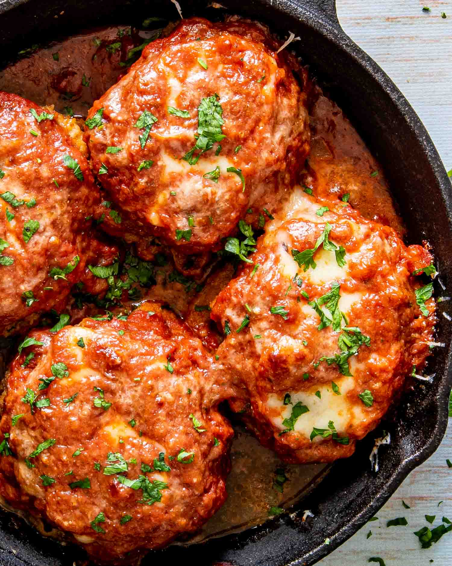 italian style hamburger steak in a cast iron skillet garnished with parsley.