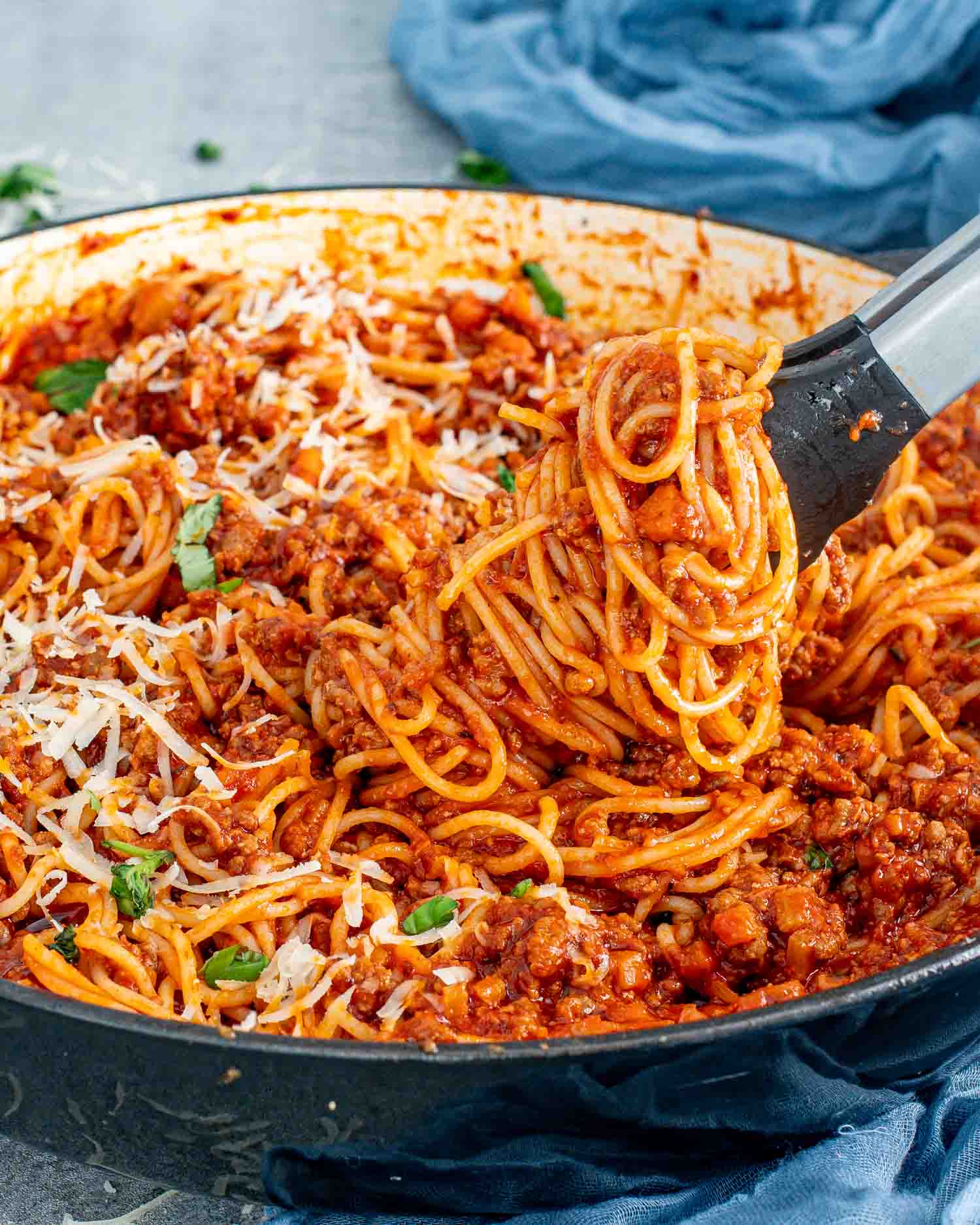 freshly made spaghetti bolognese in a pot garnished with basil and parmesan cheese.
