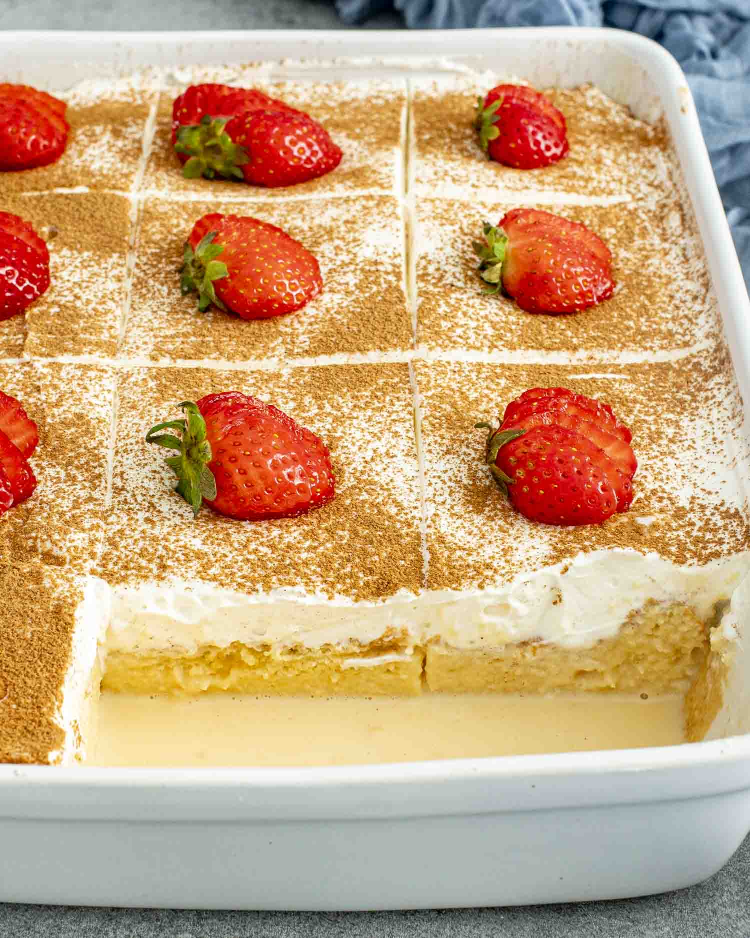 This Tres Leches Cake is sliced into squares, dusted with cinnamon, and topped with fresh strawberries, looking extra indulgent.