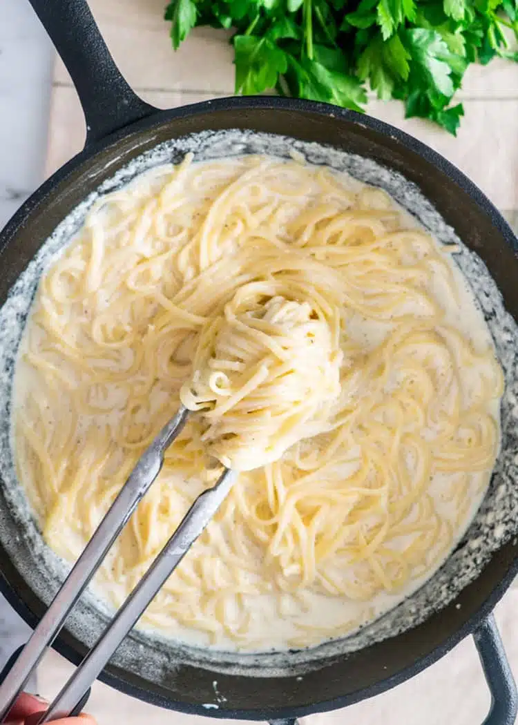 Easy Pasta Alfredo overhead shot of a pair of tongs lifting pasta alfredo out of a cast iron pan