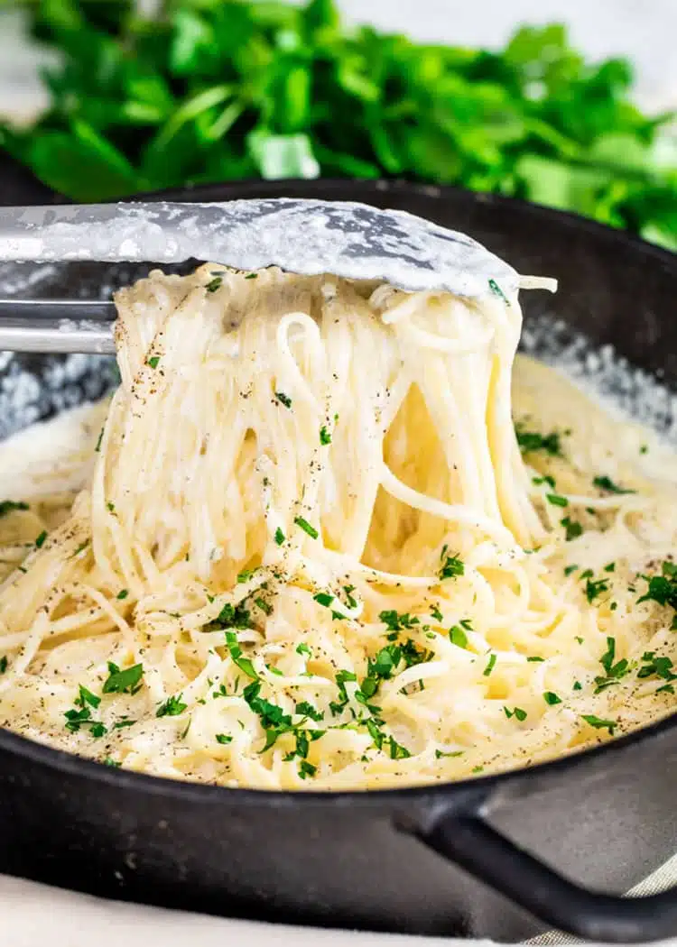 Easy Pasta Alfredo a pair of tongs lifting pasta alfredo from a cast iron pan