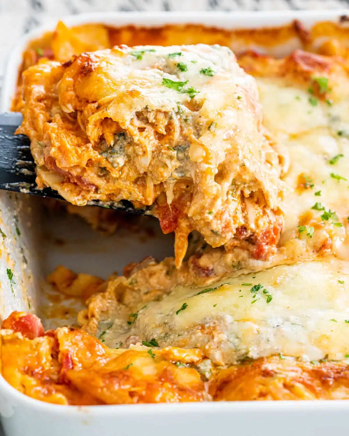 Buffalo Chicken Lasagna a spatula pulling a slice of lasagna from a casserole dish